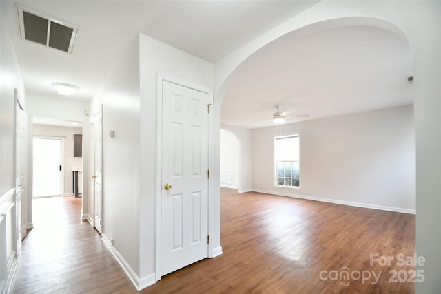 corridor featuring arched walkways, wood finished floors, visible vents, and baseboards