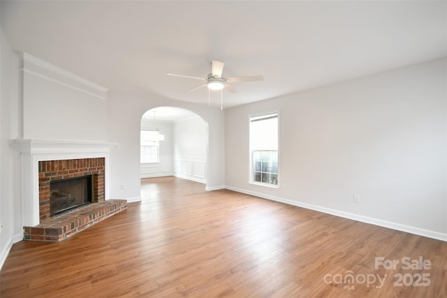 unfurnished living room featuring arched walkways, crown molding, a fireplace, ceiling fan, and wood finished floors