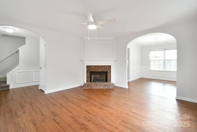 unfurnished living room with ceiling fan, wood finished floors, stairs, a fireplace, and a decorative wall