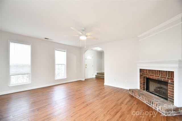 unfurnished living room featuring wood-type flooring, a brick fireplace, ornamental molding, and ceiling fan