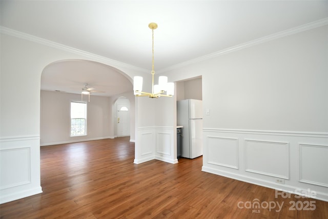 empty room featuring arched walkways, dark wood-style flooring, ceiling fan with notable chandelier, and crown molding