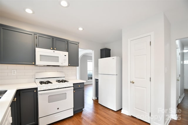 kitchen featuring arched walkways, white appliances, light countertops, and gray cabinetry