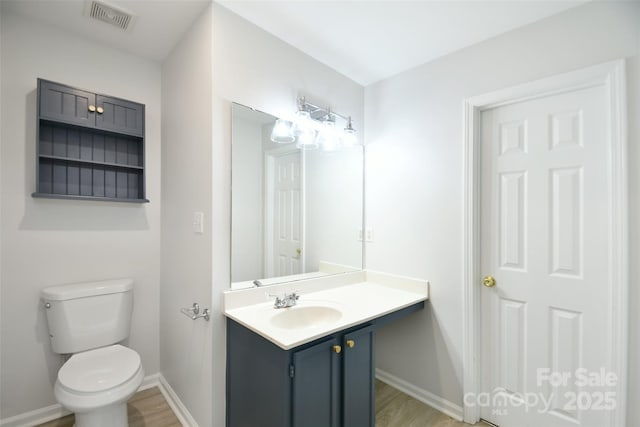 half bathroom featuring baseboards, visible vents, toilet, wood finished floors, and vanity