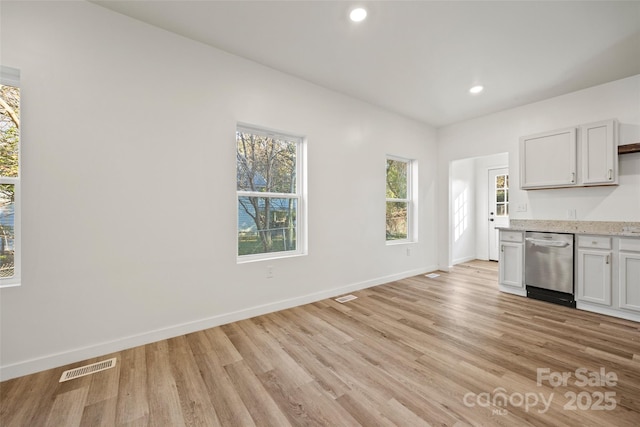 kitchen with light stone counters, white cabinetry, stainless steel dishwasher, and light hardwood / wood-style flooring