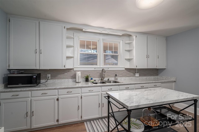 kitchen with white cabinets, light wood-type flooring, backsplash, and sink