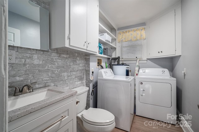 laundry area with light wood-type flooring, separate washer and dryer, sink, and water heater