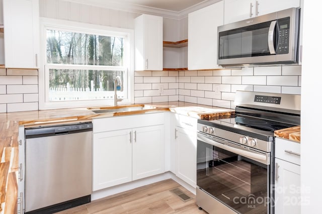 kitchen with sink, butcher block countertops, ornamental molding, stainless steel appliances, and white cabinets