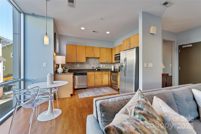 kitchen featuring sink, hanging light fixtures, light hardwood / wood-style flooring, decorative backsplash, and stainless steel appliances