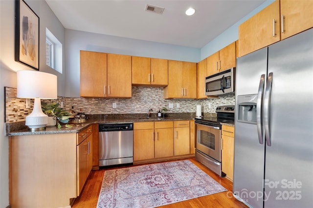 kitchen with tasteful backsplash, sink, light hardwood / wood-style flooring, and appliances with stainless steel finishes