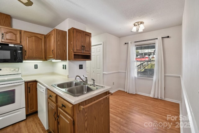 kitchen featuring kitchen peninsula, a textured ceiling, white appliances, sink, and light hardwood / wood-style flooring