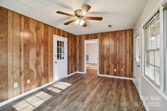 empty room featuring ceiling fan, dark hardwood / wood-style floors, and wood walls