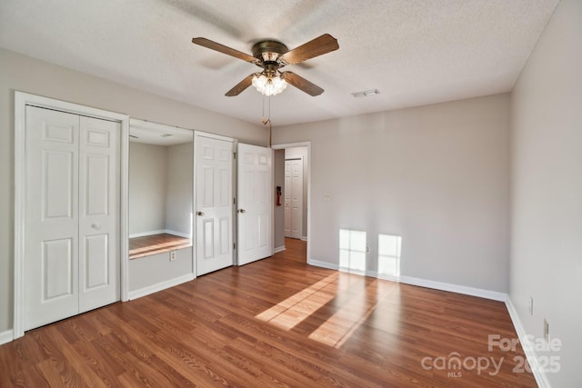 unfurnished bedroom featuring hardwood / wood-style floors, a textured ceiling, ceiling fan, and multiple closets