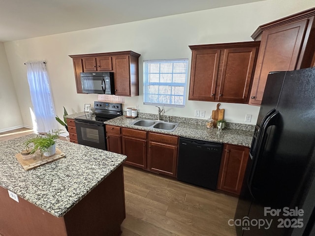 kitchen with light stone countertops, sink, black appliances, and wood-type flooring