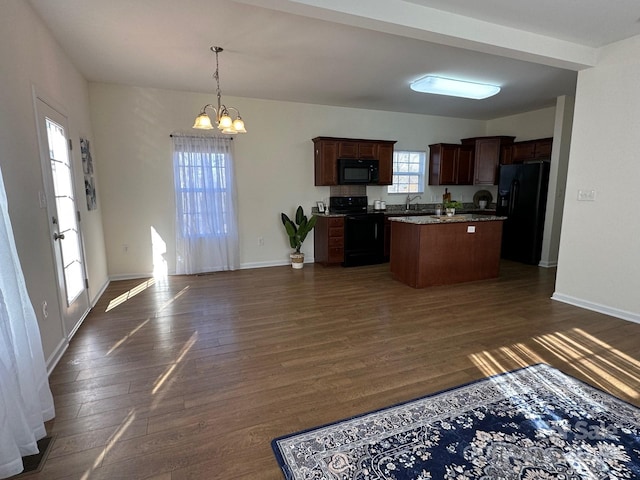 kitchen featuring dark wood-type flooring, black appliances, decorative light fixtures, a chandelier, and a kitchen island