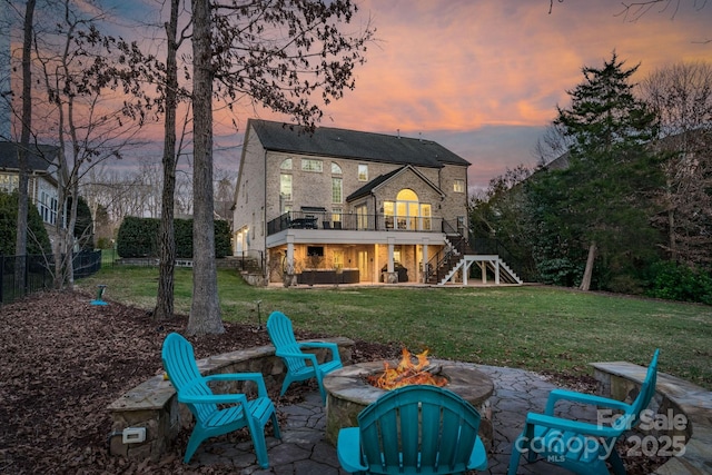 back house at dusk featuring a deck, a lawn, a patio area, and a fire pit