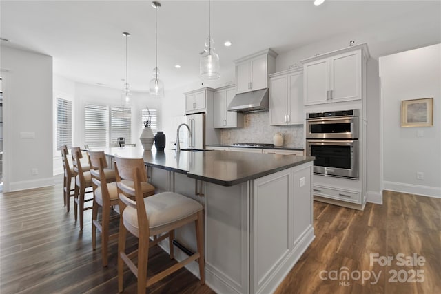 kitchen with a breakfast bar area, a center island with sink, appliances with stainless steel finishes, pendant lighting, and backsplash