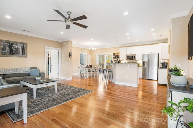 living room with ceiling fan with notable chandelier, light wood-type flooring, and crown molding