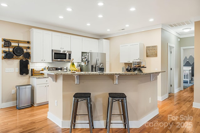 kitchen with a breakfast bar, white cabinets, an island with sink, light stone counters, and stainless steel appliances