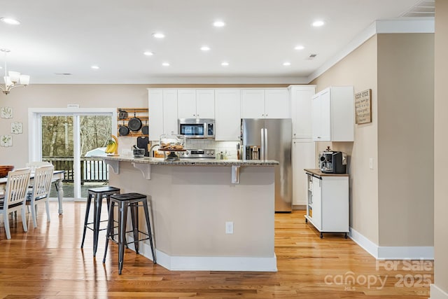 kitchen with appliances with stainless steel finishes, dark stone countertops, white cabinets, a breakfast bar area, and an island with sink