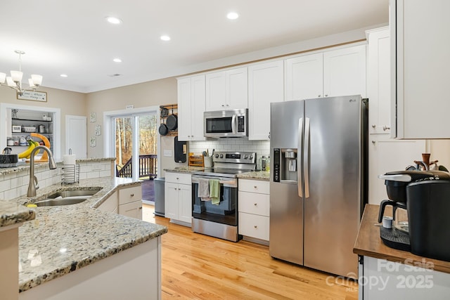 kitchen featuring white cabinetry, sink, stainless steel appliances, a notable chandelier, and pendant lighting