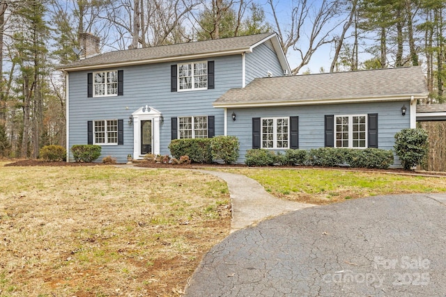 colonial inspired home with a chimney, a front yard, and a shingled roof