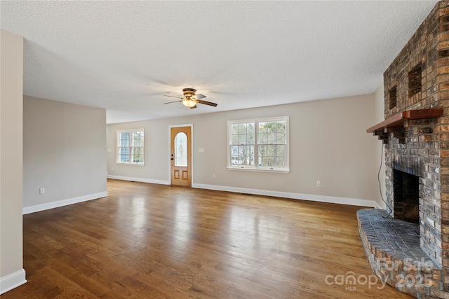 unfurnished living room with a healthy amount of sunlight, a brick fireplace, ceiling fan, and wood finished floors