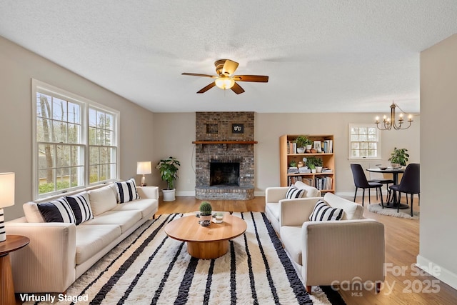 living area with ceiling fan with notable chandelier, a fireplace, a textured ceiling, and wood finished floors