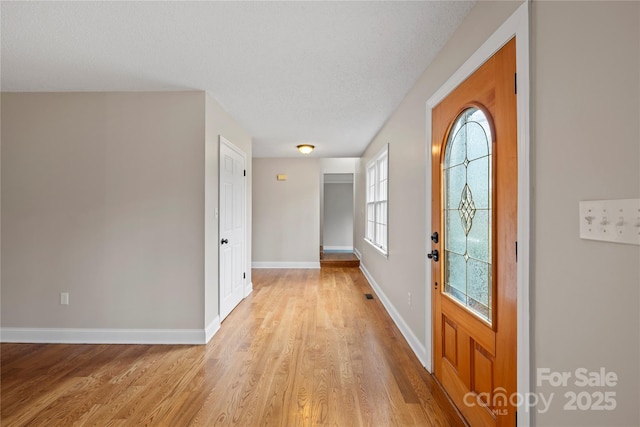 foyer entrance featuring light wood finished floors, visible vents, a textured ceiling, and baseboards