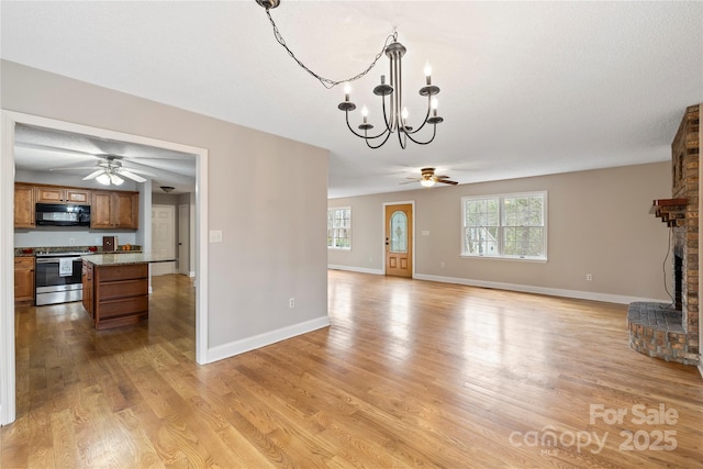 unfurnished living room featuring light wood-type flooring, baseboards, a brick fireplace, and ceiling fan with notable chandelier