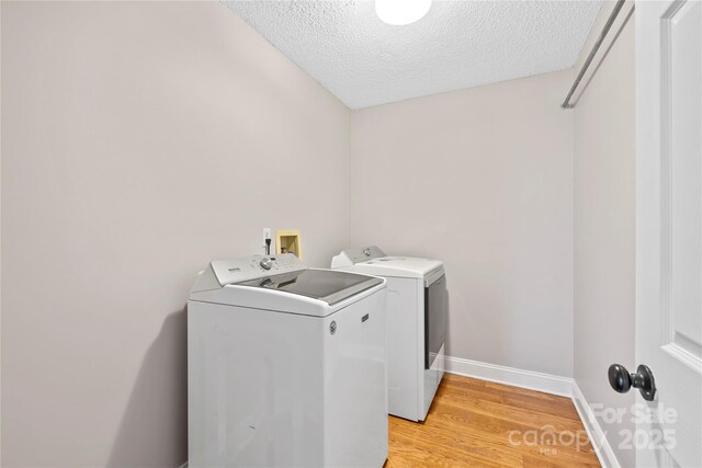 laundry room featuring baseboards, laundry area, a textured ceiling, light wood-type flooring, and washer and clothes dryer