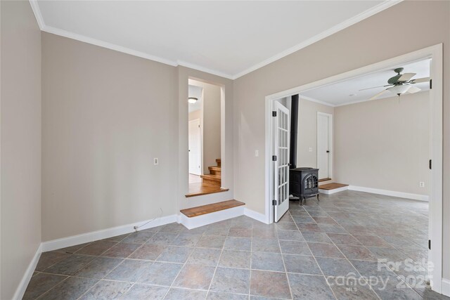 unfurnished room with stairs, baseboards, a wood stove, and crown molding