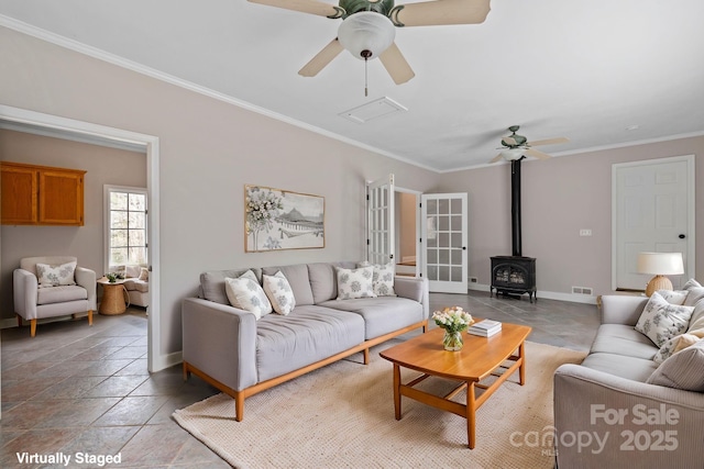 living area featuring baseboards, visible vents, a wood stove, ceiling fan, and crown molding