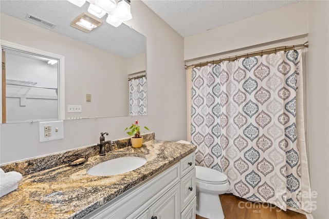 bathroom featuring visible vents, toilet, vanity, wood finished floors, and a textured ceiling