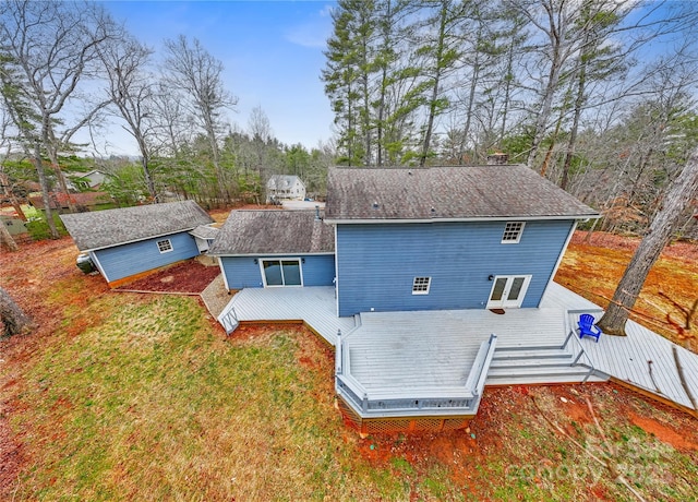 rear view of property featuring a yard, an outbuilding, a deck, and a shingled roof