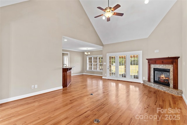 unfurnished living room with ceiling fan with notable chandelier, light hardwood / wood-style floors, and high vaulted ceiling