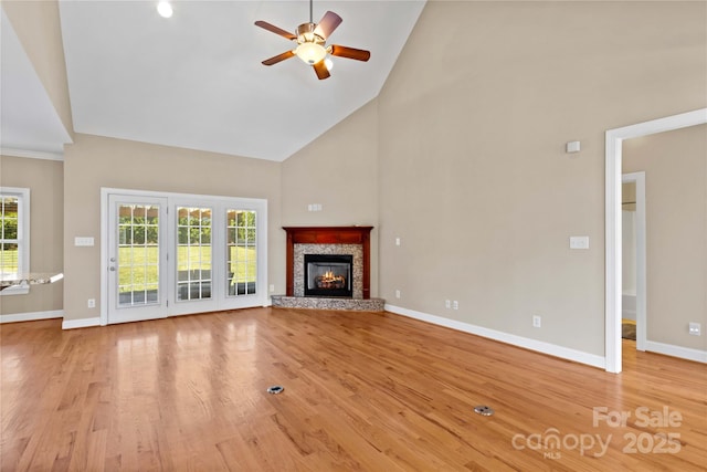 unfurnished living room with a stone fireplace, ceiling fan, high vaulted ceiling, and light wood-type flooring