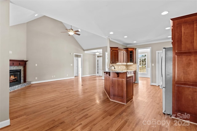 kitchen with a stone fireplace, light hardwood / wood-style flooring, decorative backsplash, ceiling fan, and a kitchen bar