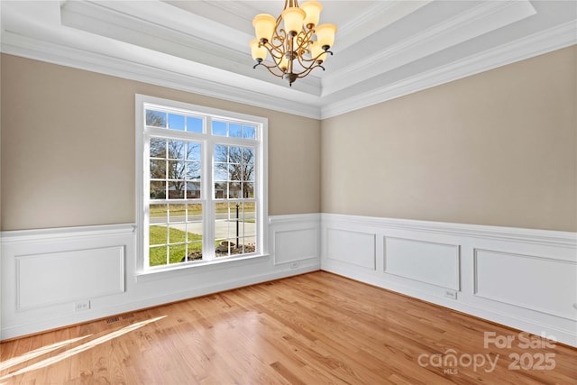 empty room with a tray ceiling, crown molding, light wood-type flooring, and an inviting chandelier