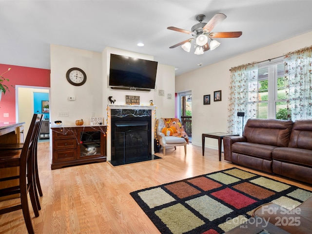 living room with a high end fireplace, hardwood / wood-style floors, a wealth of natural light, and ceiling fan