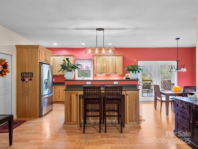 kitchen with a kitchen breakfast bar, hanging light fixtures, a kitchen island, light hardwood / wood-style floors, and stainless steel fridge with ice dispenser