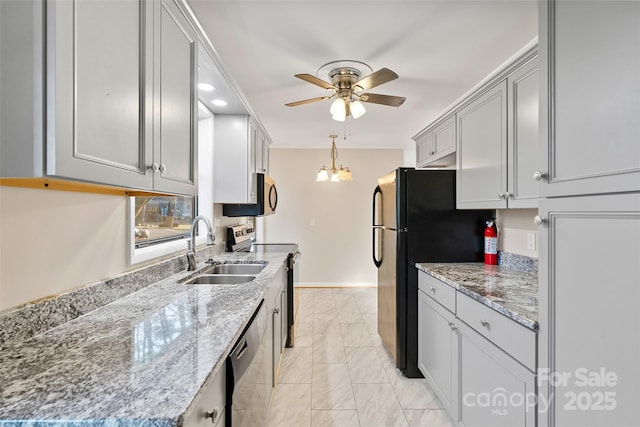 kitchen featuring light stone countertops, sink, ceiling fan with notable chandelier, and appliances with stainless steel finishes