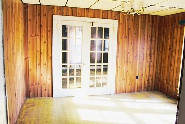 interior space with an inviting chandelier, carpet floors, wooden walls, and french doors