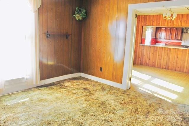 empty room with carpet flooring, a notable chandelier, and wood walls