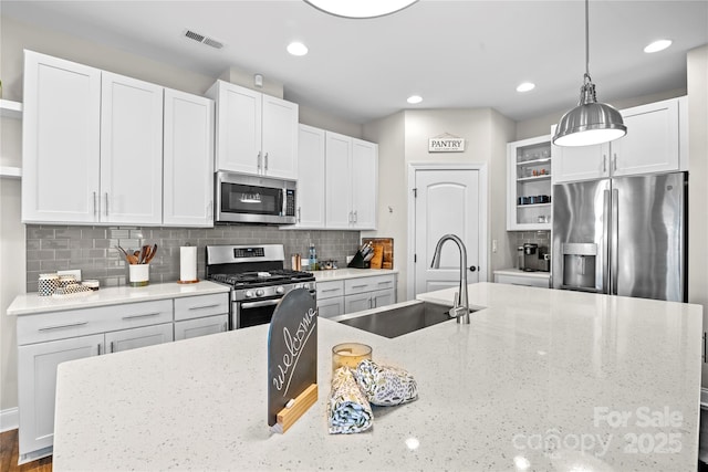 kitchen with pendant lighting, backsplash, sink, light stone countertops, and stainless steel appliances