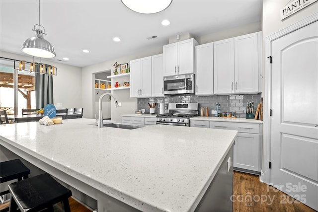 kitchen with a kitchen island with sink, white cabinets, tasteful backsplash, light stone counters, and stainless steel appliances