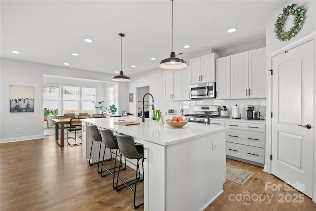 kitchen featuring appliances with stainless steel finishes, a kitchen island with sink, decorative light fixtures, white cabinets, and a breakfast bar area