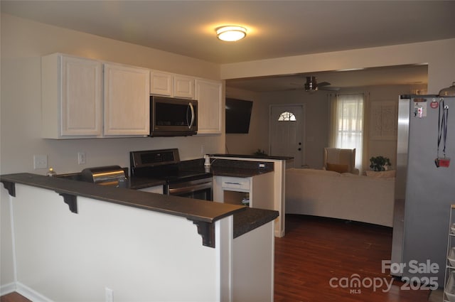 kitchen with kitchen peninsula, a kitchen bar, stainless steel appliances, ceiling fan, and white cabinetry