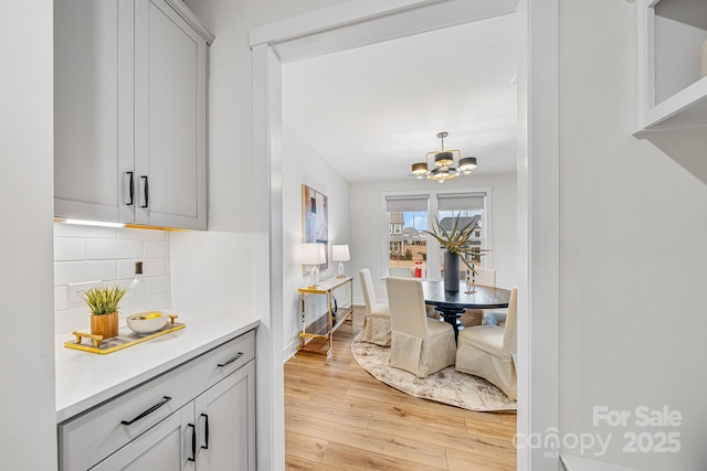 kitchen featuring decorative light fixtures, an inviting chandelier, decorative backsplash, and light hardwood / wood-style flooring