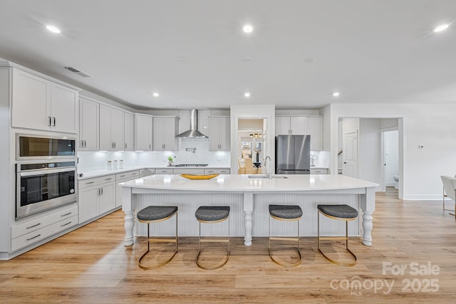 kitchen featuring white cabinets, a kitchen island with sink, appliances with stainless steel finishes, and a kitchen bar