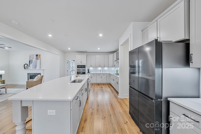 kitchen with white cabinets, light wood-type flooring, sink, a center island with sink, and stainless steel fridge